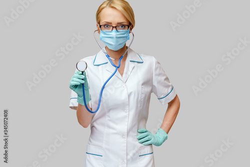 female doctor with stethoscope wearing protective mask and latex gloves over light grey background
