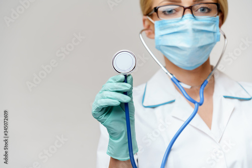 female doctor with stethoscope wearing protective mask and latex gloves over light grey background