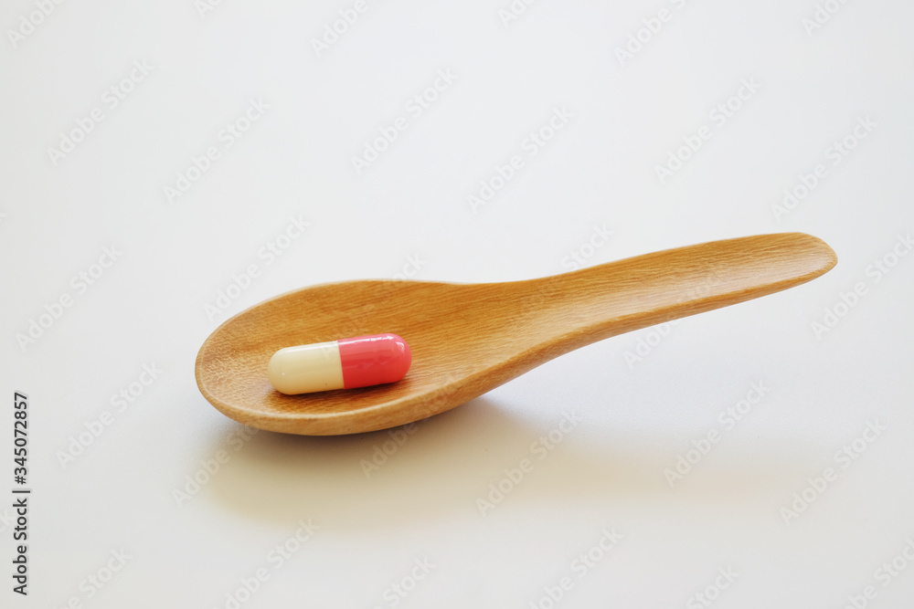 White and pink capsule or Pill in the wooden spoon isolated on white background. Medicine and healthy concept. White and pink capsule or Pill in the wooden spoon isolated on white background. Medicine and healthy concept.