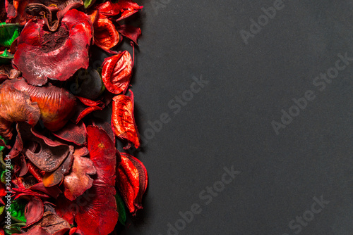 Red potpourri flowers and leaves on ceramic plate on black background, top view photo