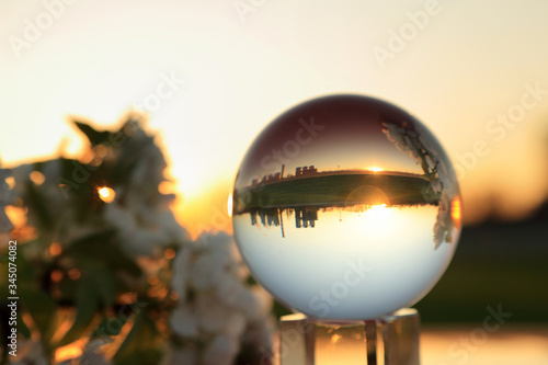 Fototapeta Naklejka Na Ścianę i Meble -  Fabryka w szklanej kuli w czasie zachodu słońca i kwiatami na gałęźi drzewa.