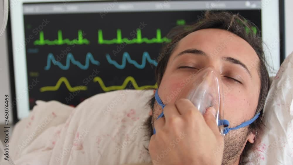 sick young man lies in an oxygen mask against the background of a monitor with graphs of vital indicators