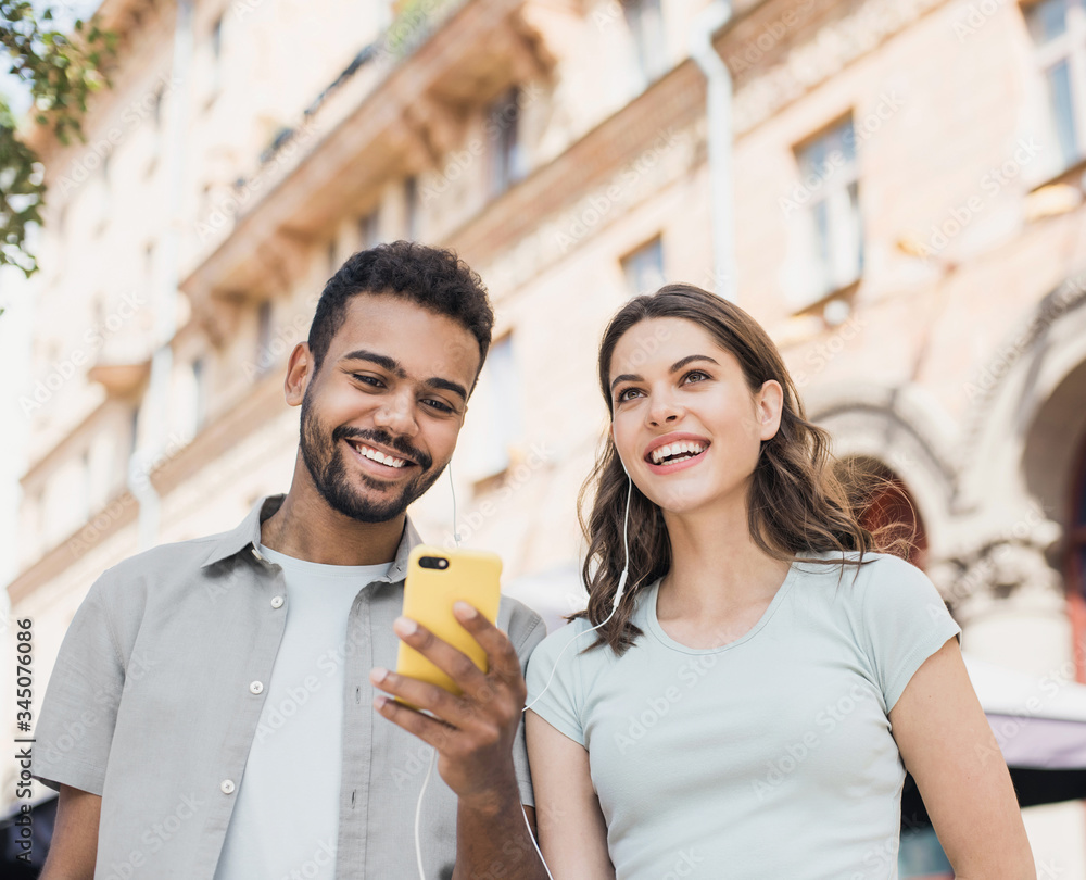 Young couple using smartphone outdoors. Joyful smiling woman and man looking at mobile phone in a city. Love, technology, connection, communication, summer travel concept
