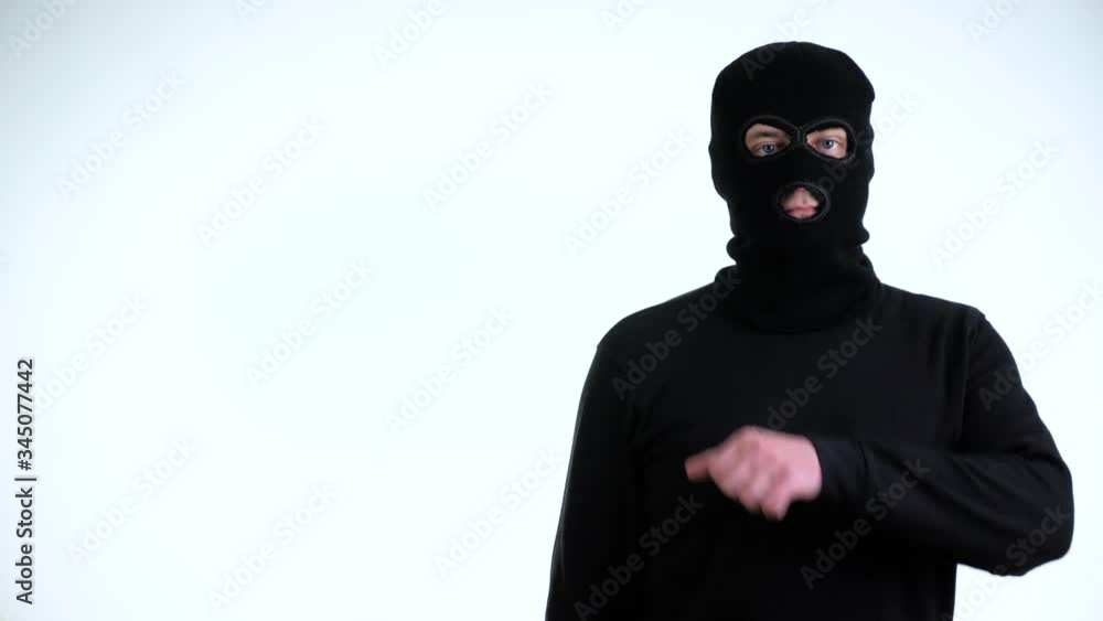 Nervous criminal man in black balaclava showing intimidating gesture - cutting throat on a white background. Nervous criminal man in black balaclava showing intimidating gesture - cutting throat on a white background.