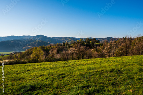 green field in the mountains with a valley below and the sun on the horizon  czech