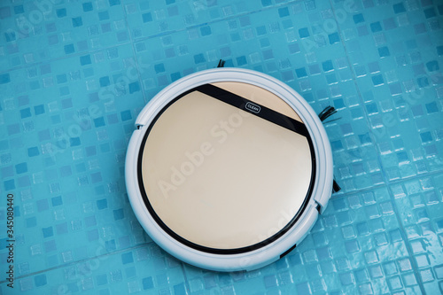 white and gold robot vacuum cleaner on the floor cleans blue tiles