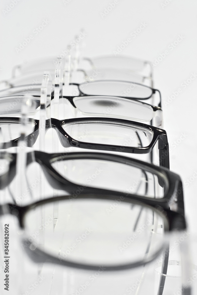 Many glasses on a white background. Glasses are stacked in a row on a transparent shop window. Glass stand on gray table. Sale and exhibition of optics. Many glasses on a white background. Glasses are stacked in a row on a transparent shop window. Glass stand on gray table. Sale and exhibition of optics.