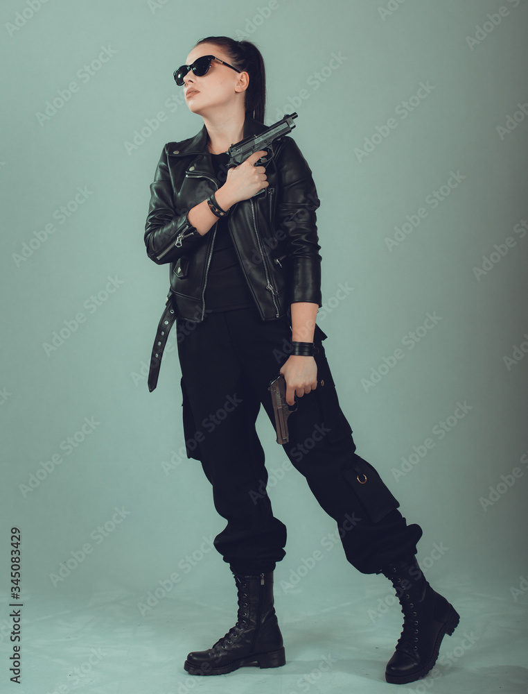 Naklejka premium Shot of a sexy military woman posing with guns,in a black jacket,black glasses in the eyes