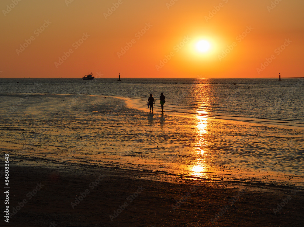 Beautiful and colorful sunset with silhouettes of two people walking by the sea. Sundown in a beach in Sanlucar de Barrameda, Cádiz, Andalucia, Spain.