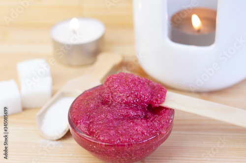 Natural pink body scrub made from sugar. Pink scrub in a glass cup on a background of candles and sugar.