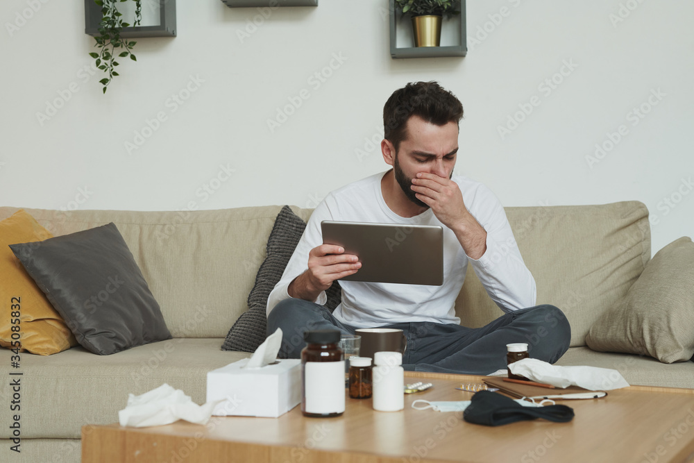 Very sick young man with digital tablet covering his mouth while coughing Very sick young man with digital tablet covering his mouth while coughing