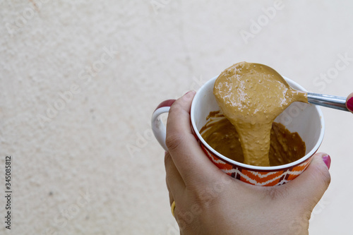 Valokuva a girl showing thick hand beaten coffee paste in a colorful mug against plain wa