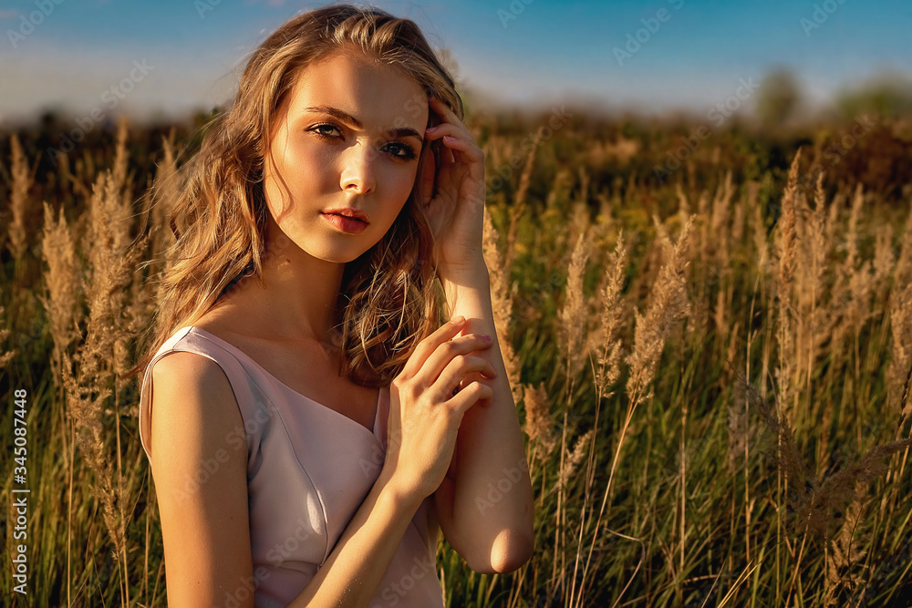 Portrait of a blond girl in a dress that sits in a field with tall grass and a birch. Portrait of a blond girl in a dress that sits in a field with tall grass and a birch.