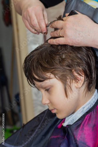 A female hairdresser cuts a boy's hair with scissors