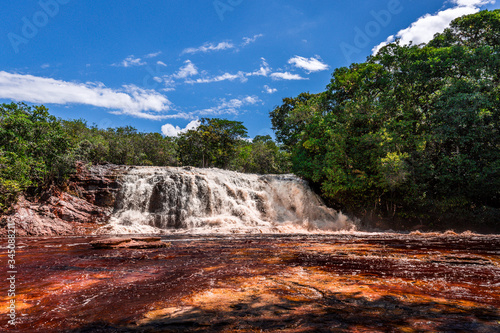 Red water at the stunning Presidente Figueiredo waterfall (Reserva Ecológica Cachoeira Santuário) surrounded by green rainforest on a clear blue sunny day near Manaus, Amazon in Brazil, South America