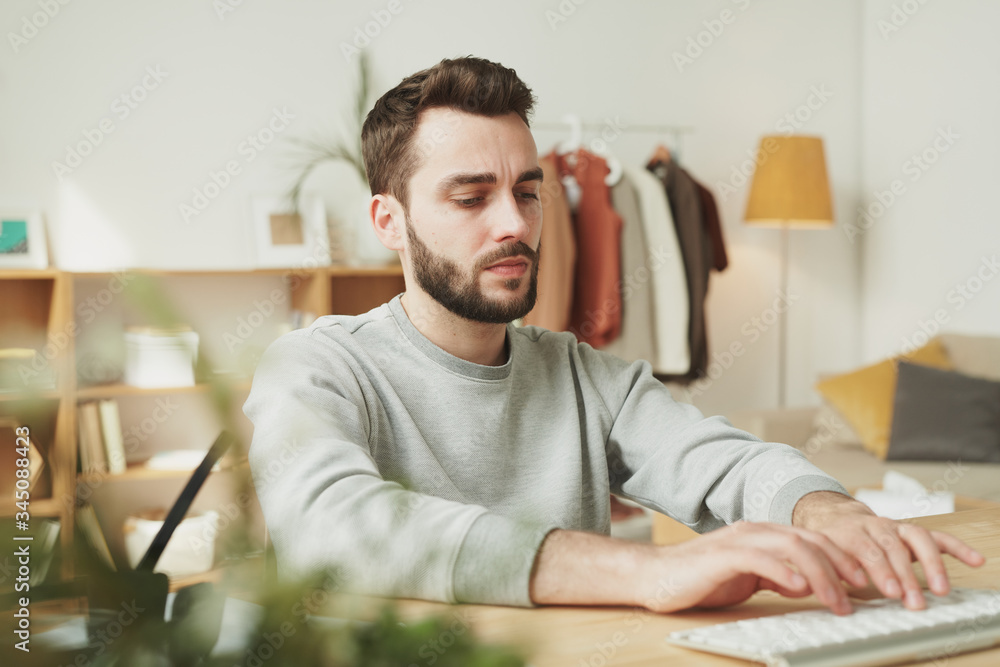 Obraz premium Serious young businessman in grey sweatshirt typing in front of laptop