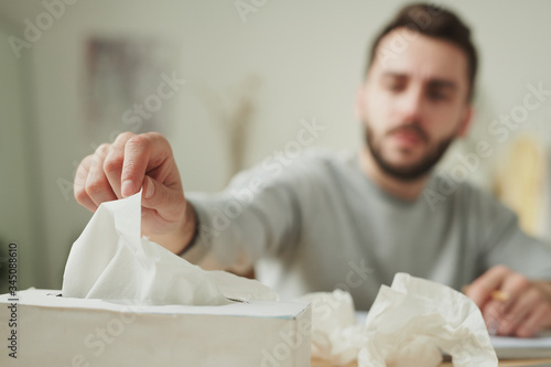 Hand of sick businessman taking paper tissue from box while sitting by table
