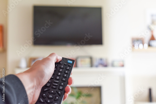 Hand with tv remote control switching television on at home