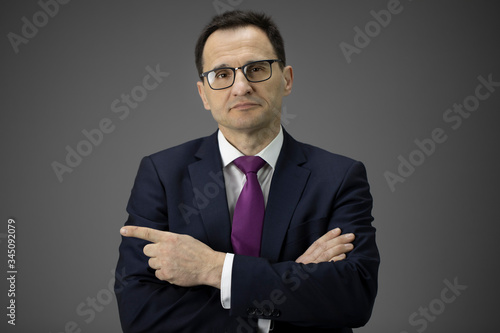 confident crossed-handed 40s businessman in glasses pointing at copy space with his forefinger isolated on gray background. business bank offer, sale, insurance, investment, technology, high quality
