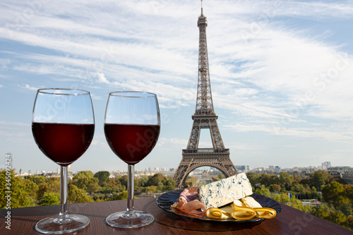 Wallpaper Mural Two glasses of red wine with charcuterie assortment on view of Paris and Eiffel tower. Glass of red wine with different snacks - plate with ham, sliced, blue cheese. Couple romantic celebration. Torontodigital.ca