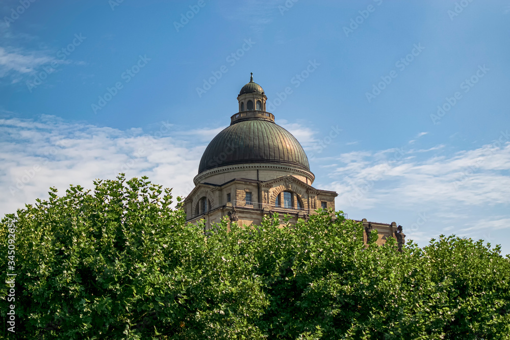 View of the Dome of the Bavarian State Chancellery from behind one of the bushes in the park. Photograph taken in Munich, Bavaria, Germany.