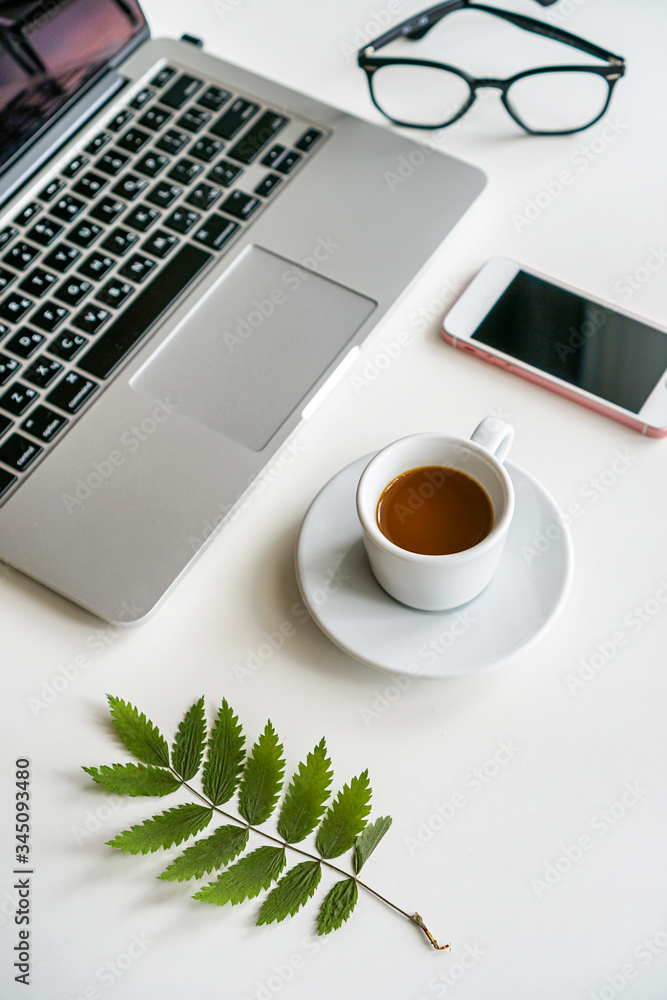 on the table is a mug with coffee and a laptop, next to it are a notebook, glasses and a green sheet on the table is a mug with coffee and a laptop, next to it are a notebook, glasses and a green sheet