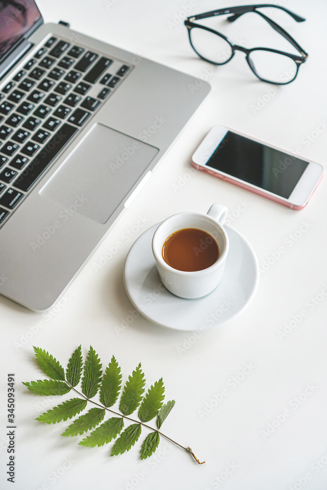 on the table is a mug with coffee and a laptop, next to it are a notebook, glasses and a green sheet on the table is a mug with coffee and a laptop, next to it are a notebook, glasses and a green sheet