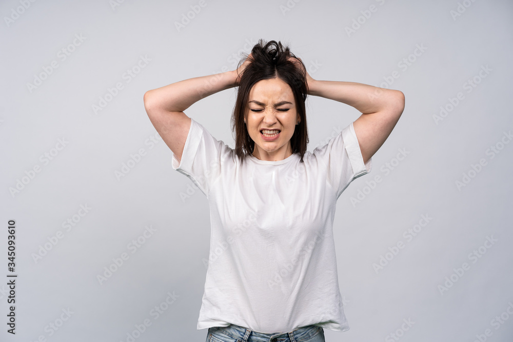 Girl in white shirt on white background, gritted his teeth and squeezed two his head in his hands, the concept of negative emotions, illness Girl in white shirt on white background, gritted his teeth and squeezed two his head in his hands, the concept of negative emotions, illness