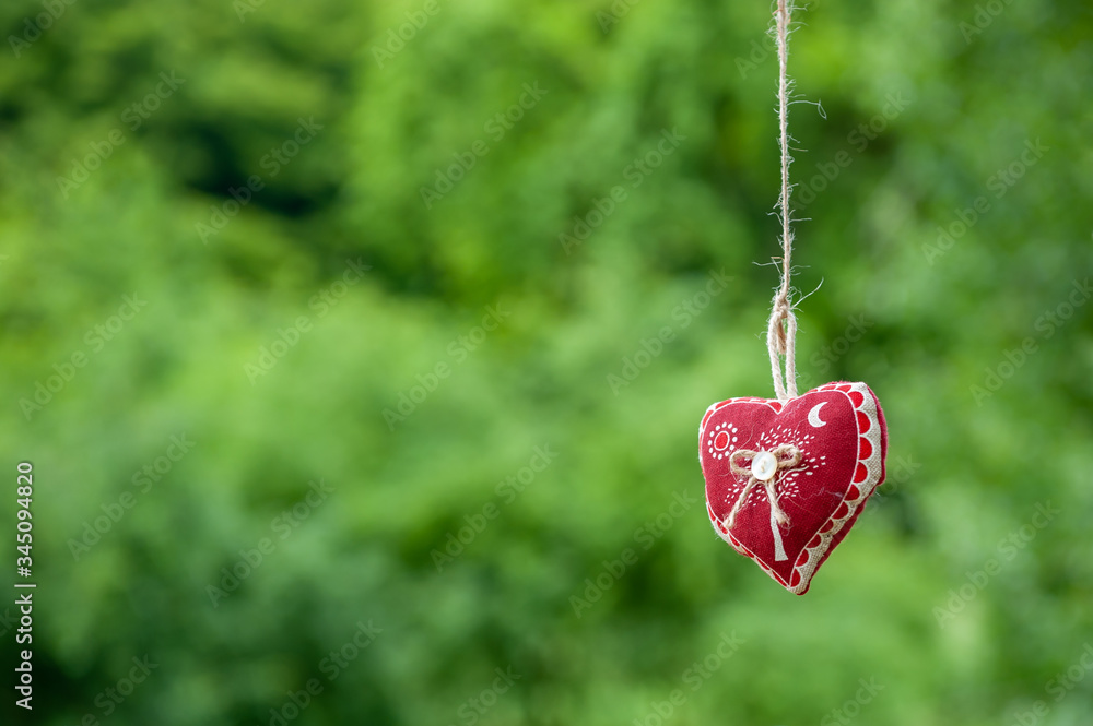 Isolated handmade cotton fabric heart hanging on bast string on green grass background. Red fabric heart hanging on the clothesline. Summer wedding theme. Love and valentine in nature. Isolated handmade cotton fabric heart hanging on bast string on green grass background. Red fabric heart hanging on the clothesline. Summer wedding theme. Love and valentine in nature.
