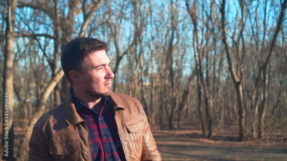 Portrait of a guy in a leather jacket on a background of a spring park. A smiling guy enjoys the upcoming spring, looks at the sun and covers it with his palm. Portrait of a guy in a leather jacket on a background of a spring park. A smiling guy enjoys the upcoming spring, looks at the sun and covers it with his palm.