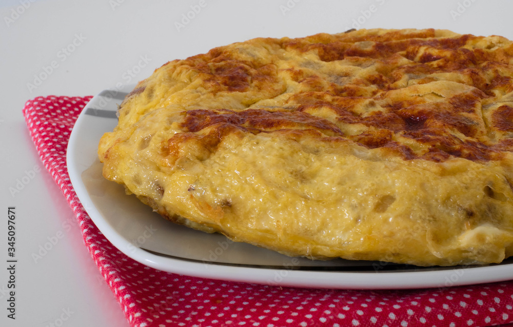 Spanish omelete on a white plate and red rug on white background