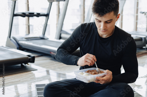 stylish guy in the gym relaxing on the floor and eating healthy food.