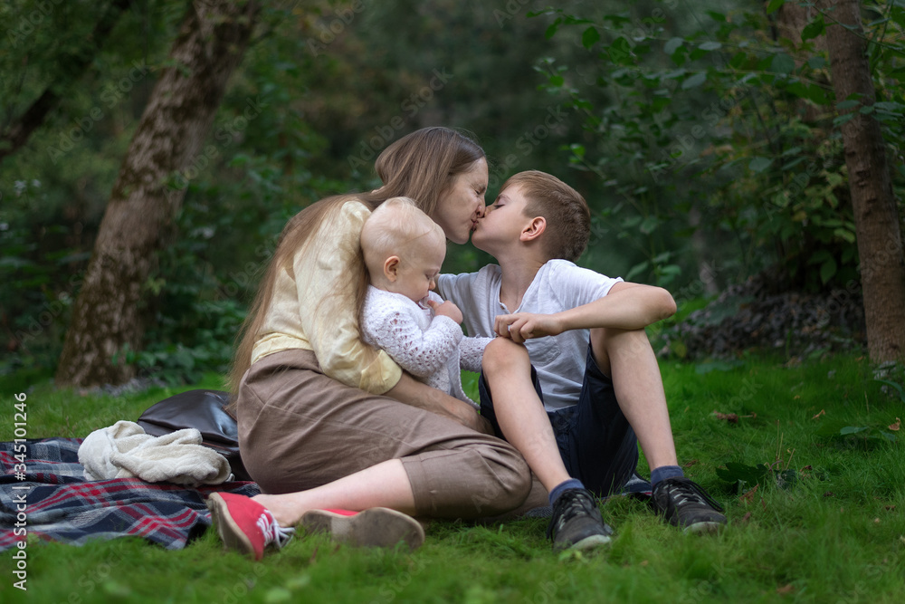 Happy family at picnic. Young mother kisses her older son and holding baby
