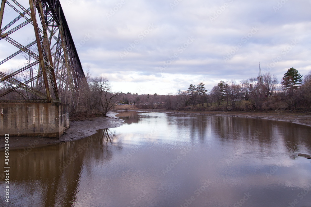 Fototapeta premium View of the 1859 St-Félix-de-Valois Church on a hill and the 1908 railway trestle bridge over the Cap-Rouge River seen during an early spring morning, Quebec City, Quebec, Canada