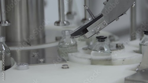 glass bottles filled and sealed with rubber caps on a medical solution conveyor line aluminium cap packaging section close up medical industry