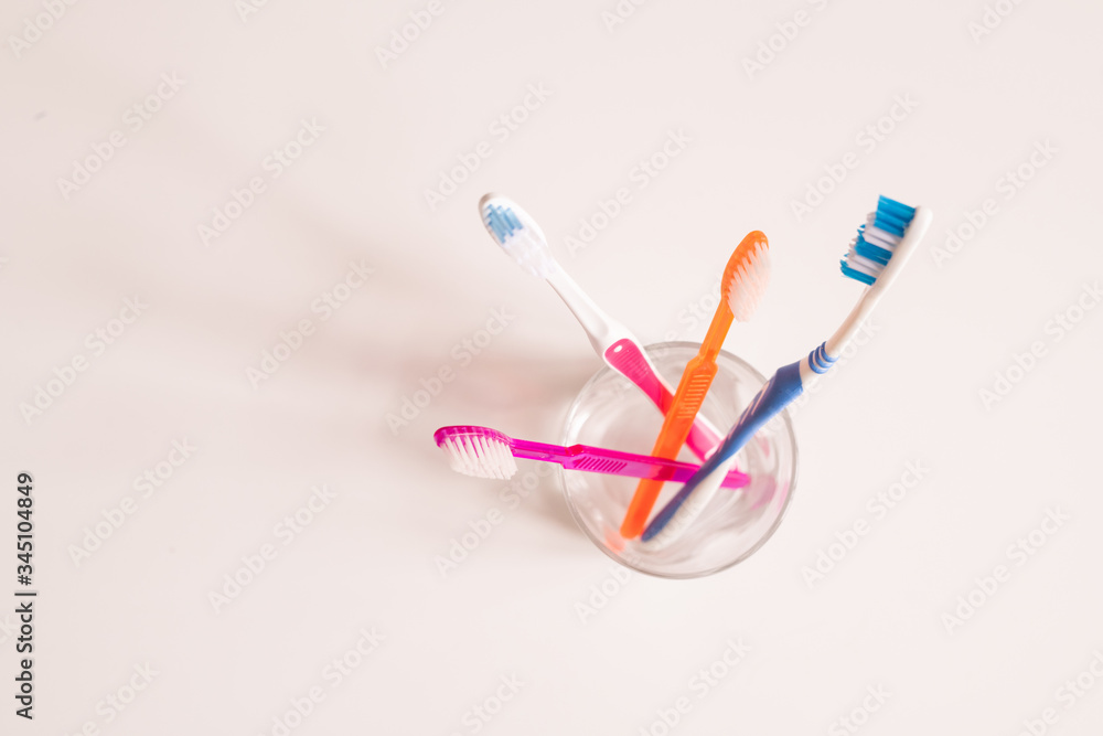 Overview of glass with bunch of new blue, orange and pink toothbrushes Overview of glass with bunch of new blue, orange and pink toothbrushes