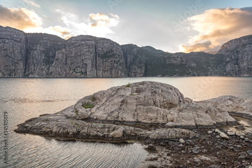 Stone island in the water of a fjord, surrounded by a mountain range at sunset photo