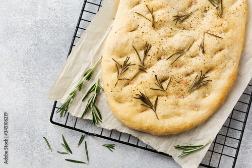 Fotografija Italian traditional focaccia bread baking with aromatic seasonings and rosemary on a light gray background