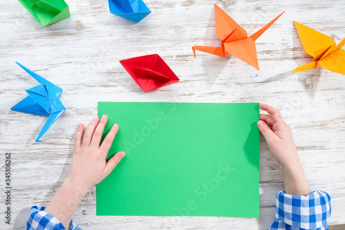 Hands with origami on the table. The child makes origami from colored paper.
