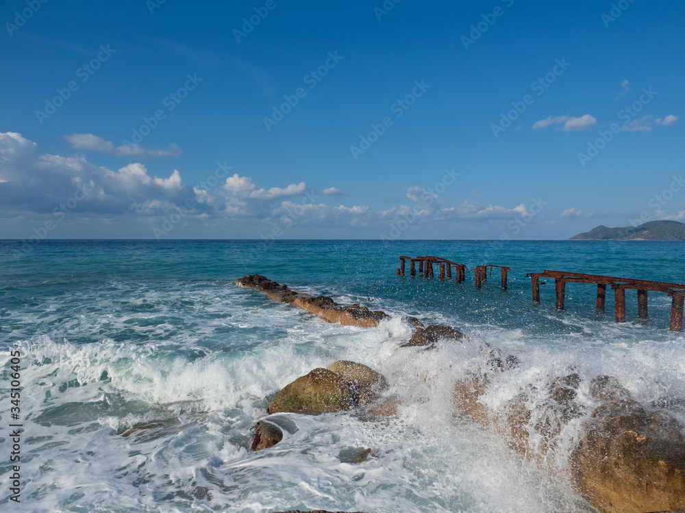 Fototapeta premium Waves breaking on a pier on a sunny day. White foam and splash of sea waves.