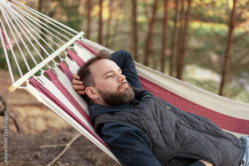 young male hipster with a beard in a hammock on nature in the forest, rest in the park