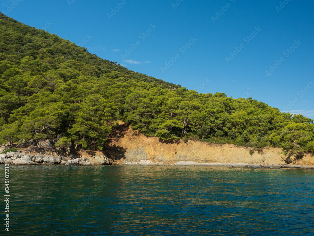View of the coast from the sea. Amazing color of water, beautiful rocks with trees growing on them. Bright sunny summer day.