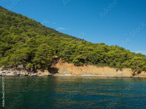 View of the coast from the sea. Amazing color of water, beautiful rocks with trees growing on them. Bright sunny summer day. © Elena