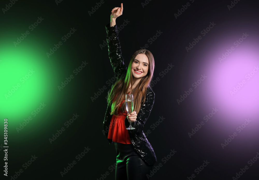 Fototapeta premium Happy young woman with glass of champagne on dark background