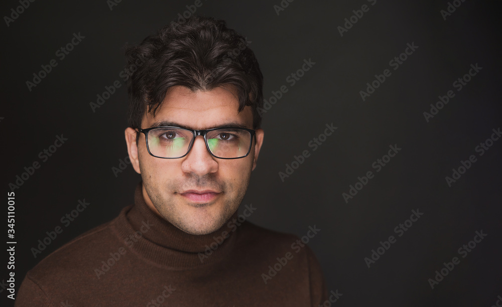 a young dark man in glasses and a turtleneck is smiling against a dark background a young dark man in glasses and a turtleneck is smiling against a dark background