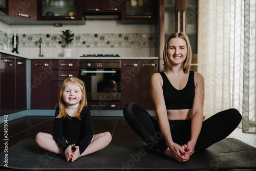 Mom and daughter on mat in yoga pose at home. Sports mom with kid doing work-out. Mum  child do the exercises  healthy family. Fitness. Calmness concept. Coronavirus Stay Home. Trains during pandemic.