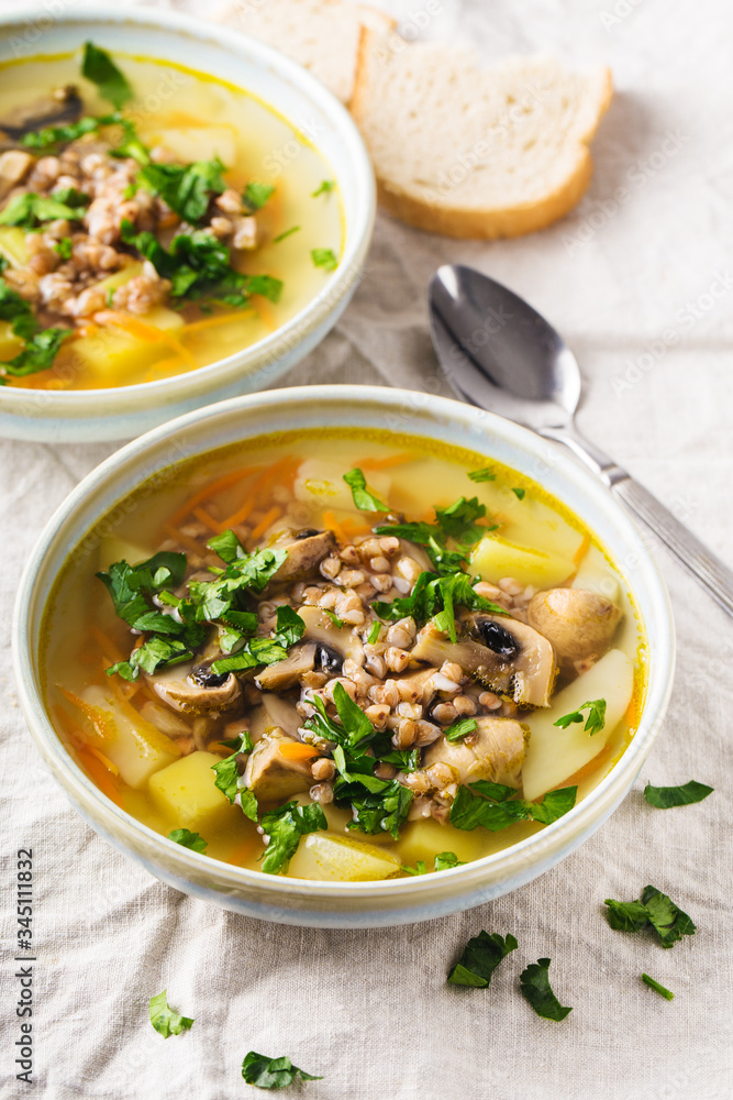Soup of mushrooms, buckwheat, potatoes and carrots with herbs in bowls with slice of white bread on the side, light background, vertical format.Top view Soup of mushrooms, buckwheat, potatoes and carrots with herbs in bowls with slice of white bread on the side, light background, vertical format.Top view