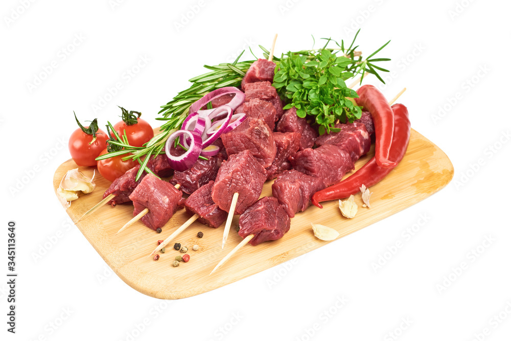 Meat skewers on bamboo skewers, with young basil, rosemary, red pepper, garlic and cherry tomatoes lie on a cutting board on a white background. Meat skewers on bamboo skewers, with young basil, rosemary, red pepper, garlic and cherry tomatoes lie on a cutting board on a white background.