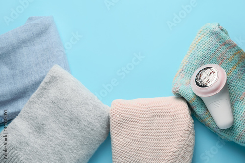 Modern fabric shaver and clothes on color background