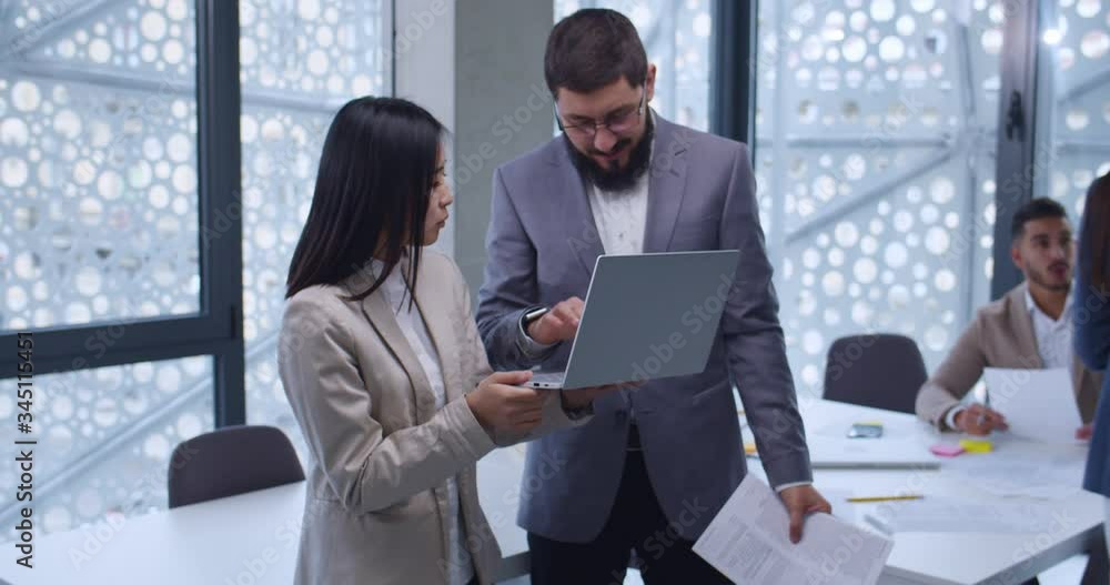 Camera zooming in on Caucasian man in glasses and Asian woman standing in office and discussing business issues. Male boss talking with young female employee and giving advices for work. Camera zooming in on Caucasian man in glasses and Asian woman standing in office and discussing business issues. Male boss talking with young female employee and giving advices for work.